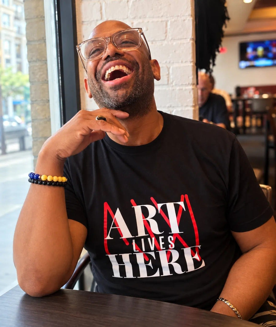 Corey Wesley, the artist behind Milton Wes Art, laughing at a table in an Art Lives Here T-shirt.