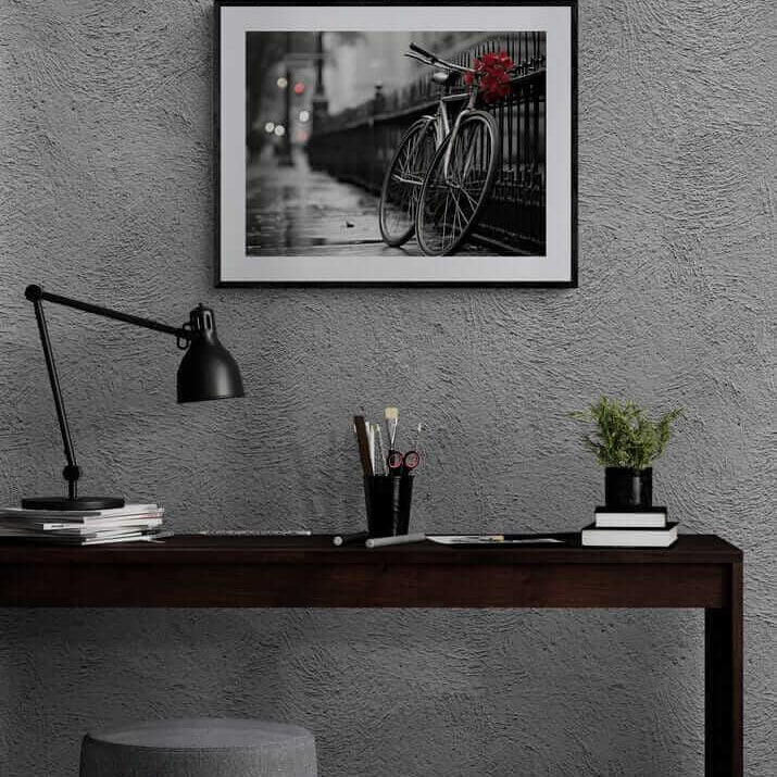 Red Floral Bicycle Print in black frame on gray wall above dark wood desk with black lamp and potted plant, modern African-American art