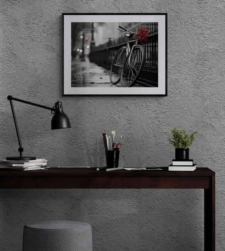 Red Floral Bicycle Print in black frame on gray wall above dark wood desk with black lamp and potted plant, modern African-American art