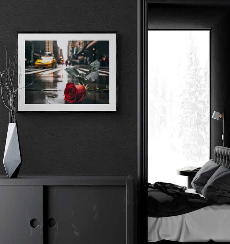 Framed poster of a red rose on a rainy NYC street, displayed on a dark wall in a modern bedroom, promoting Afrocentric home decor and colorful wall art.