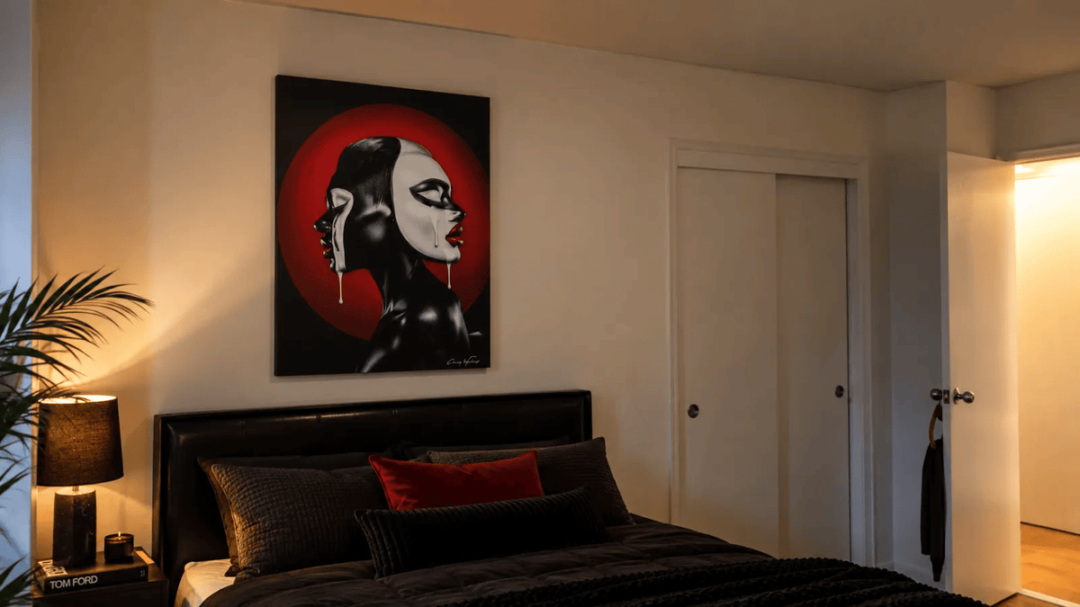 Two-Faced by Corey Wesley hanging above a black bed with red accent pillows.